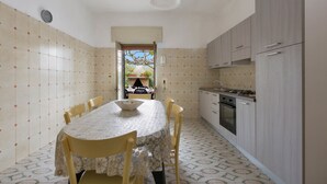Een kleine keuken met een eethoek, met een betegelde spatwand, een ingebouwde oven en een uitzicht door een open doorgang.