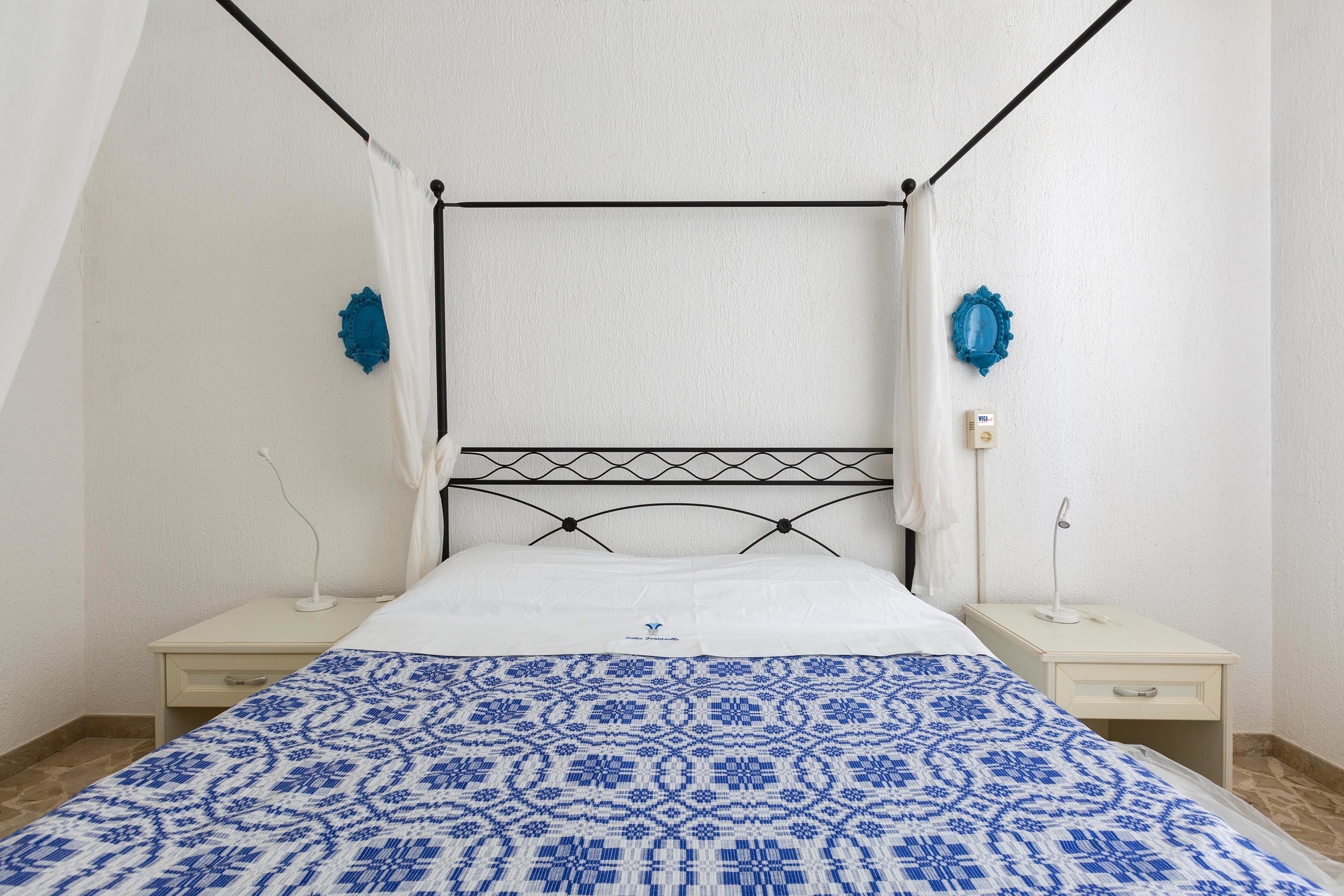 A single bed with a patterned bedspread, a bedside table with a lamp, and a wall-mounted heater.