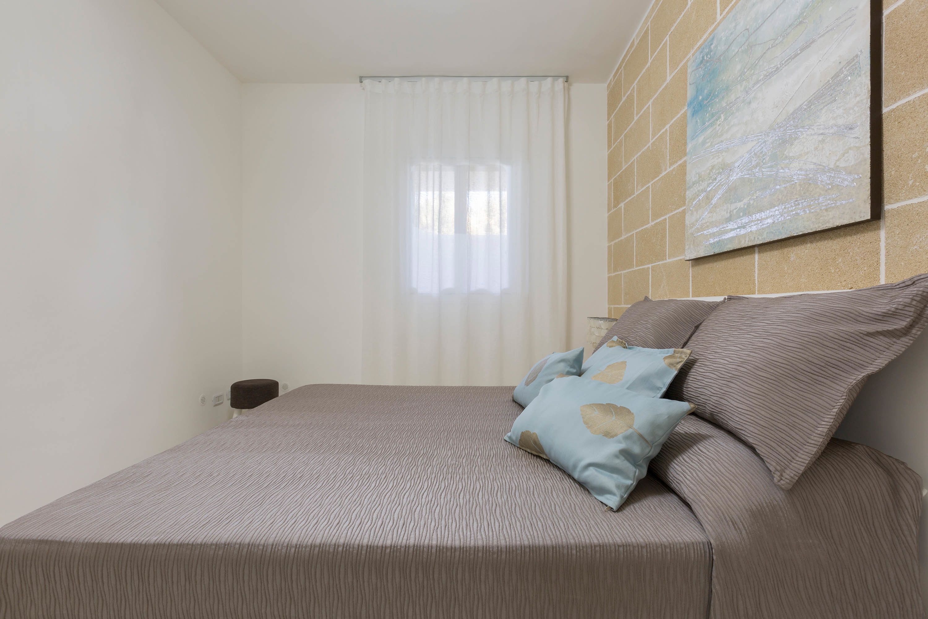 Un dormitorio con cama, ventana con cortinas, un cuadro colgado en la pared y una mesita de noche.