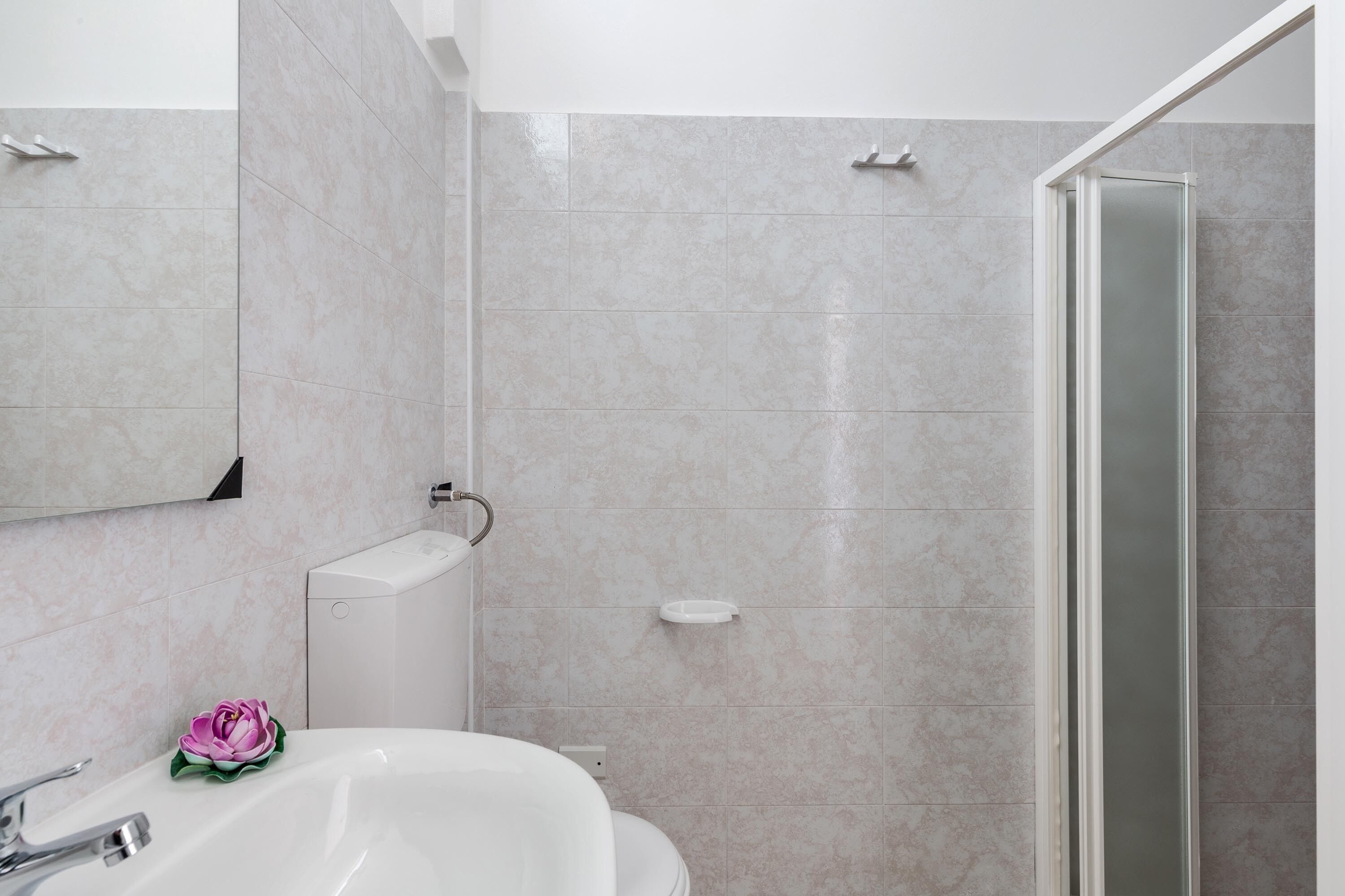 A bathroom with a white sink, a toilet, a mirror, and a shower area.