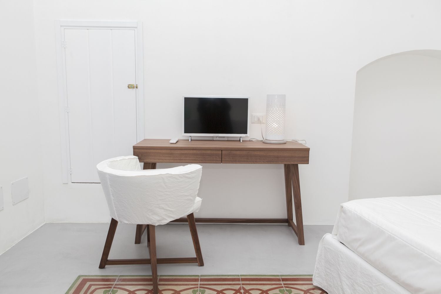 A bedroom with a bed, a desk with a computer, a chair, and a bedside table.