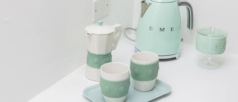 A kitchen setup with a white countertop, a white kettle, and matching cups and a glass on a tray.
