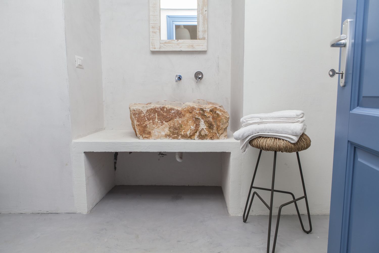 A bathroom with a white sink, a stone countertop, a mirror, and a stool with towels.