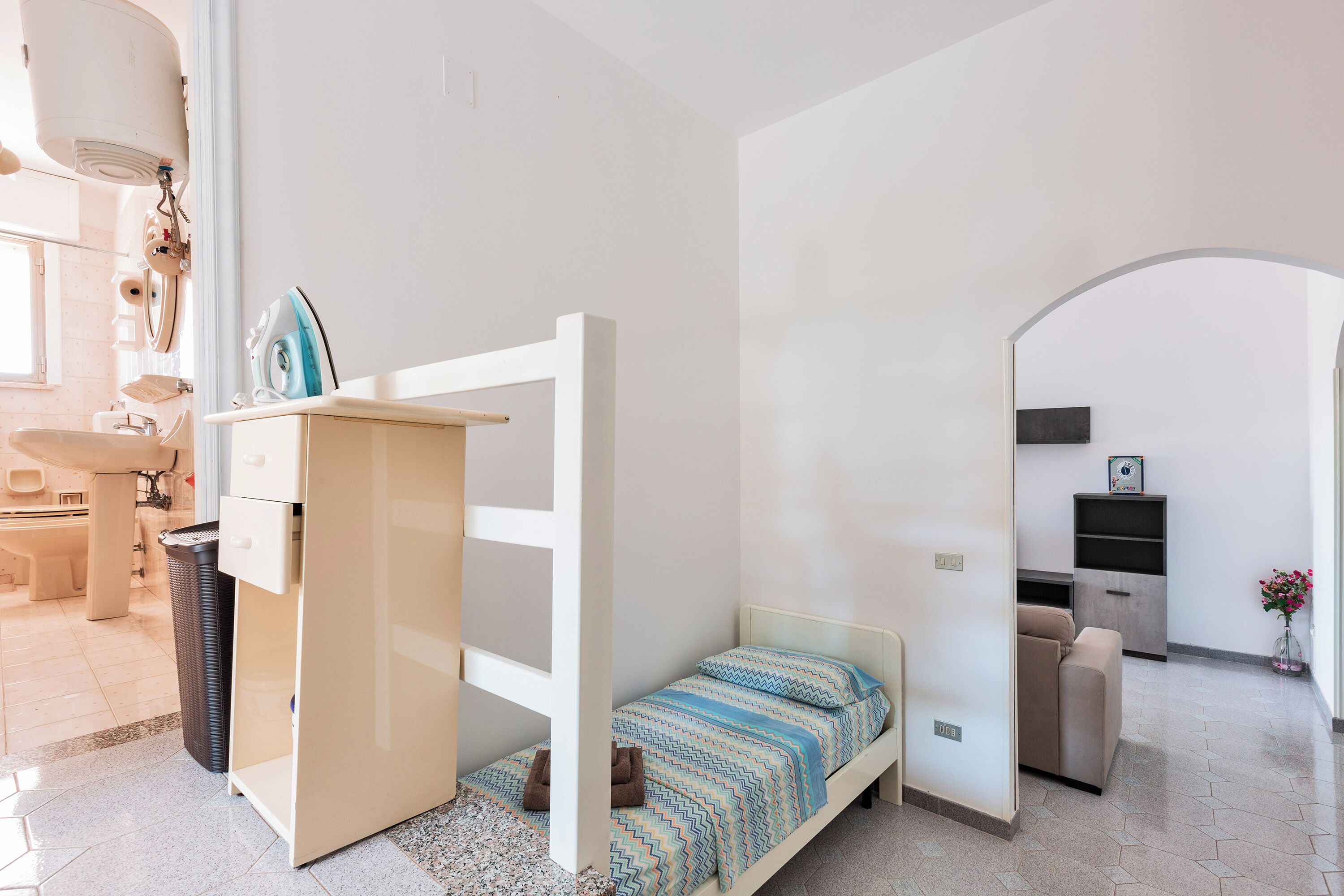 A bedroom with a bunk bed, a desk, a chair, a sofa, a small table, and a trash bin.