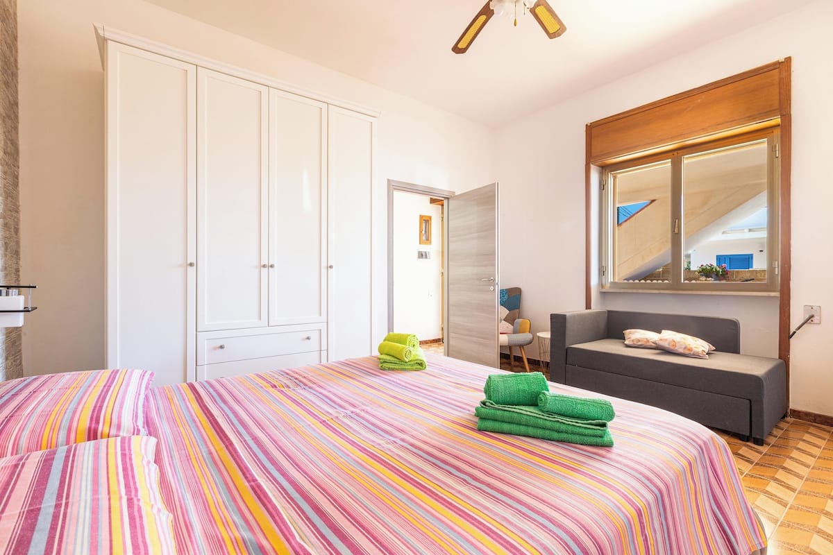 A bedroom with a large bed, a wardrobe, a grey sofa, and a mirror.