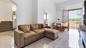 En moderne stue med en hjørnesofa, et spiseområde med bord og stole, og en trappe til et andet niveau.