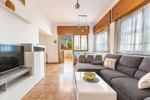 Un salon moderne avec un téléviseur à écran plat, un canapé gris et un coin repas à l’arrière-plan.