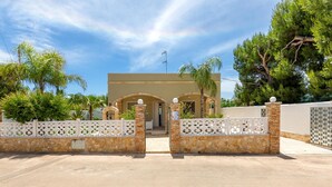 A gated entrance with a stone wall and decorative white fence, leading to a building with arched doorways and a flat roof. - Villino delle Orchidee (Nardò)