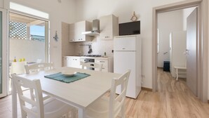 A modern kitchen with white cabinetry, a built-in stove, and a refrigerator. There is a dining table with chairs and a blue placemat. - Villino delle Orchidee (Nardò)