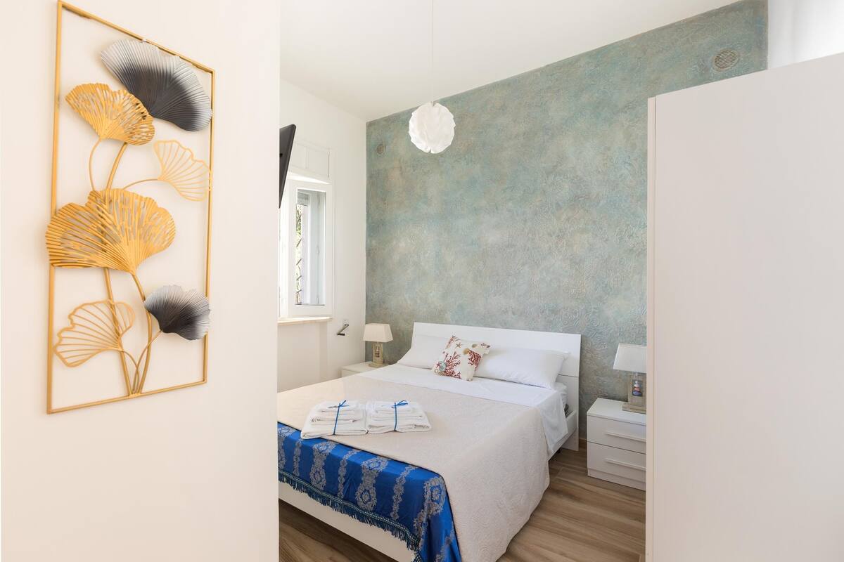 A bedroom with a bed, bedside tables, a wall art piece, and a textured wall.