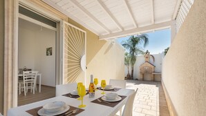 An outdoor dining area with a white table set for two, including plates, cutlery, and yellow wine glasses. - Villino delle Orchidee (Nardò)