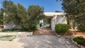 A modern building with a concrete facade, a glass door entrance, and a gravel driveway. - Villa Carlita (Carovigno)