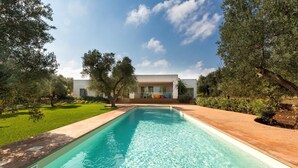 A rectangular swimming pool with clear water, surrounded by a well-maintained lawn and trees. - Villa Carlita (Carovigno)