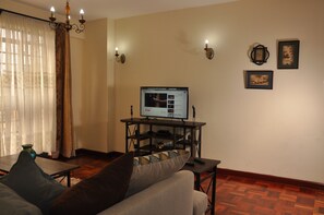A living room with a sofa, a TV on a stand, a chandelier, and wall-mounted lights.