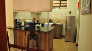A compact kitchen with a wooden countertop, a coffee maker, a microwave, a sink, and a refrigerator. - Sherry Homes - Fahari I (Nairobi)