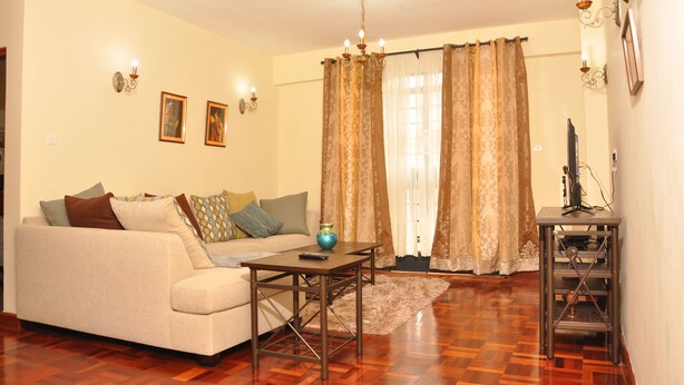 A living room with a sofa, a coffee table, a rug, and curtains. - Sherry Homes - Fahari I (Nairobi)