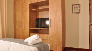 A bedroom with a bed, a wooden wardrobe, a television, and a framed picture on the wall. - Sherry Homes - Fahari I (Nairobi)