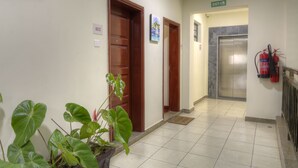 A hotel hallway with wooden doors, a fire extinguisher, and a sign indicating an exit. - Sherry Homes - Fahari I (Nairobi)