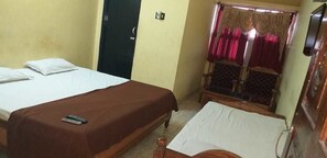 Une chambre avec deux lits, l’un recouvert d’une couvre-lit marron et l’autre d’une couvre-lit blanche. On y trouve une chaise avec un coussin, une table en bois avec une télécommande, et une fenêtre avec des rideaux.