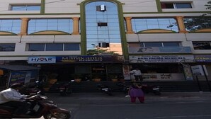Un immeuble à plusieurs étages, doté d’une entrée centrale flanquée de deux colonnes. L’immeuble présente un style architectural moderne, avec de grandes fenêtres et un toit plat.