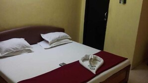 Un lit simple avec une literie blanche et un plaid rouge, une armoire noire et un appareil de climatisation fixé au mur.