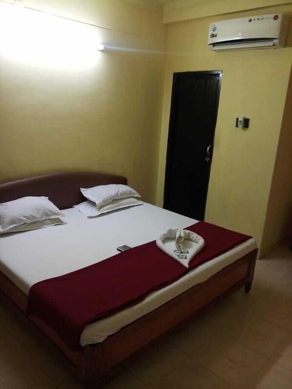 A single bed with white bedding and a red throw blanket, a black wardrobe, and an air conditioning unit on the wall.