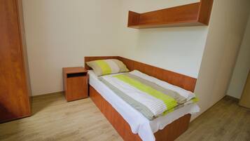 A bedroom with a wooden bed, a nightstand, a wooden wardrobe, and a shelf above the bed.