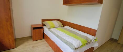 A bedroom with a wooden bed, a nightstand, a wooden wardrobe, and a shelf above the bed.