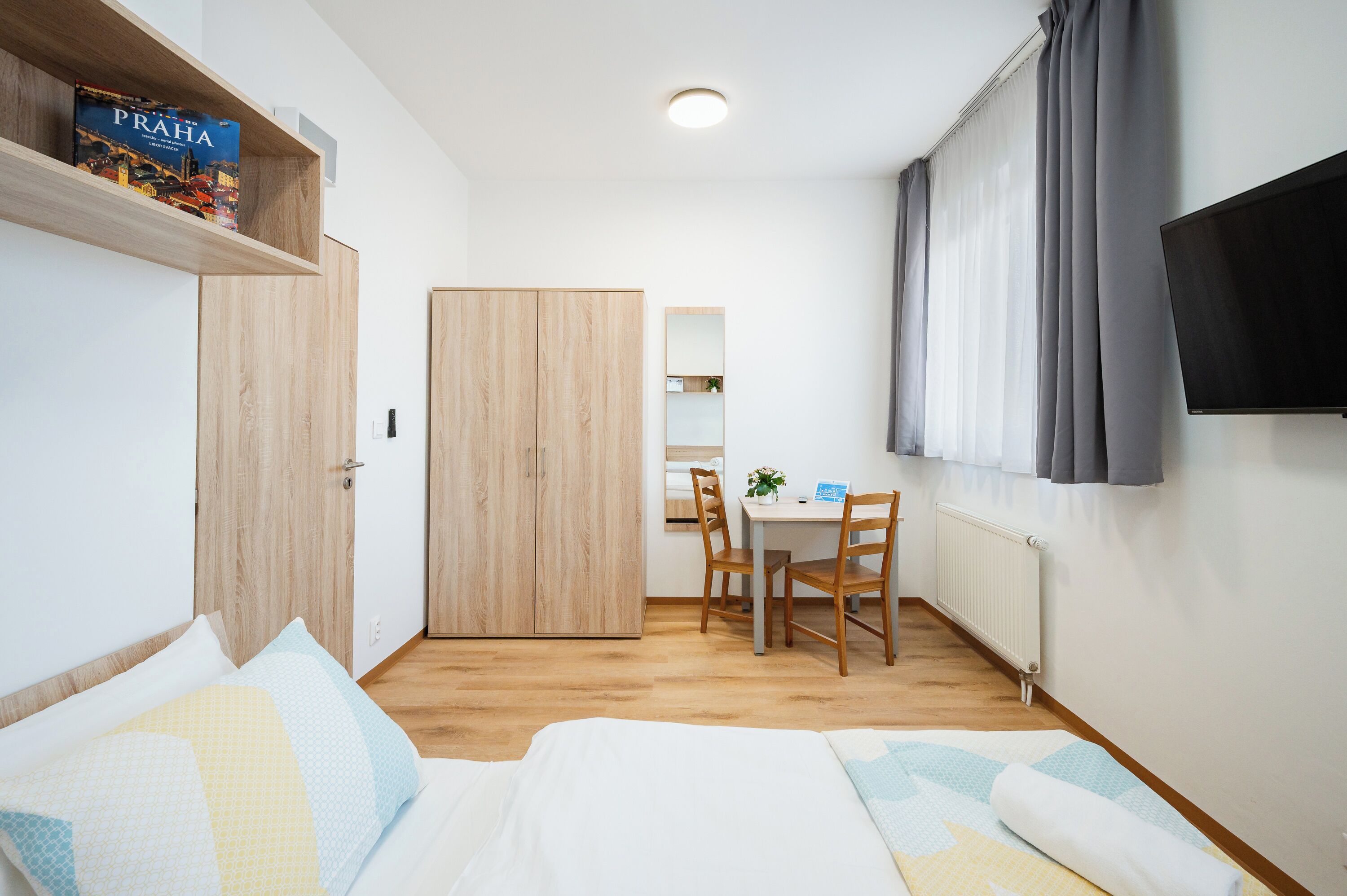 Ein Schlafzimmer mit einem Bett, einem Schreibtisch, einem Stuhl, einem Fernseher, einem Kleiderschrank und einem Regal mit einem Buch.