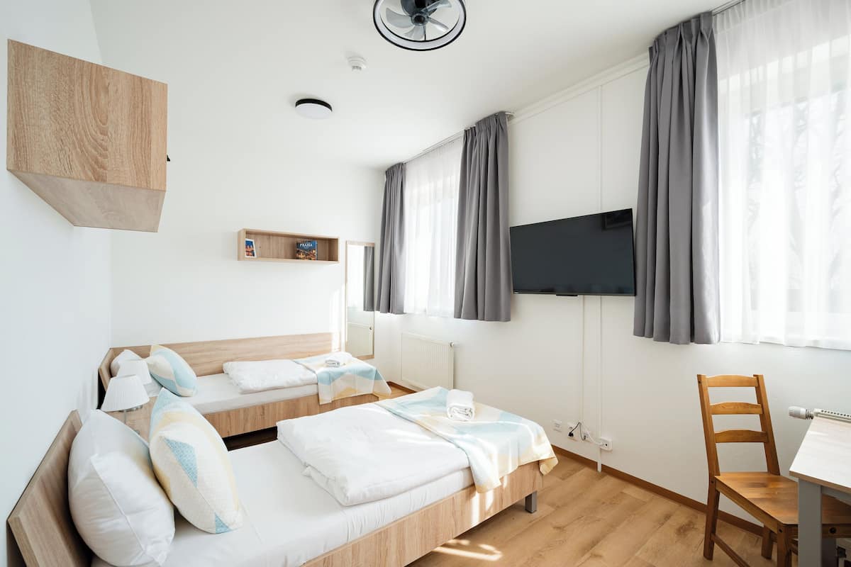 A modern hotel room with two beds, a desk, a chair, a TV, and a window with curtains.