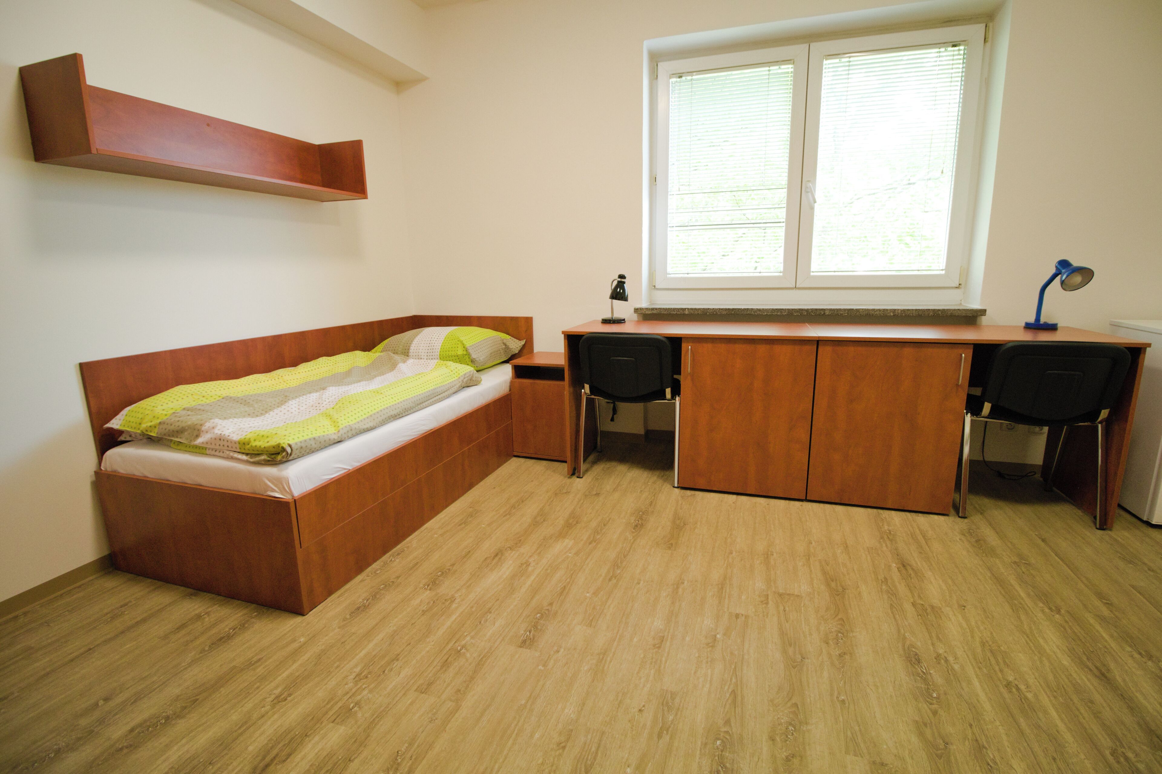 A bedroom with a bed, desk, chair, and a window.