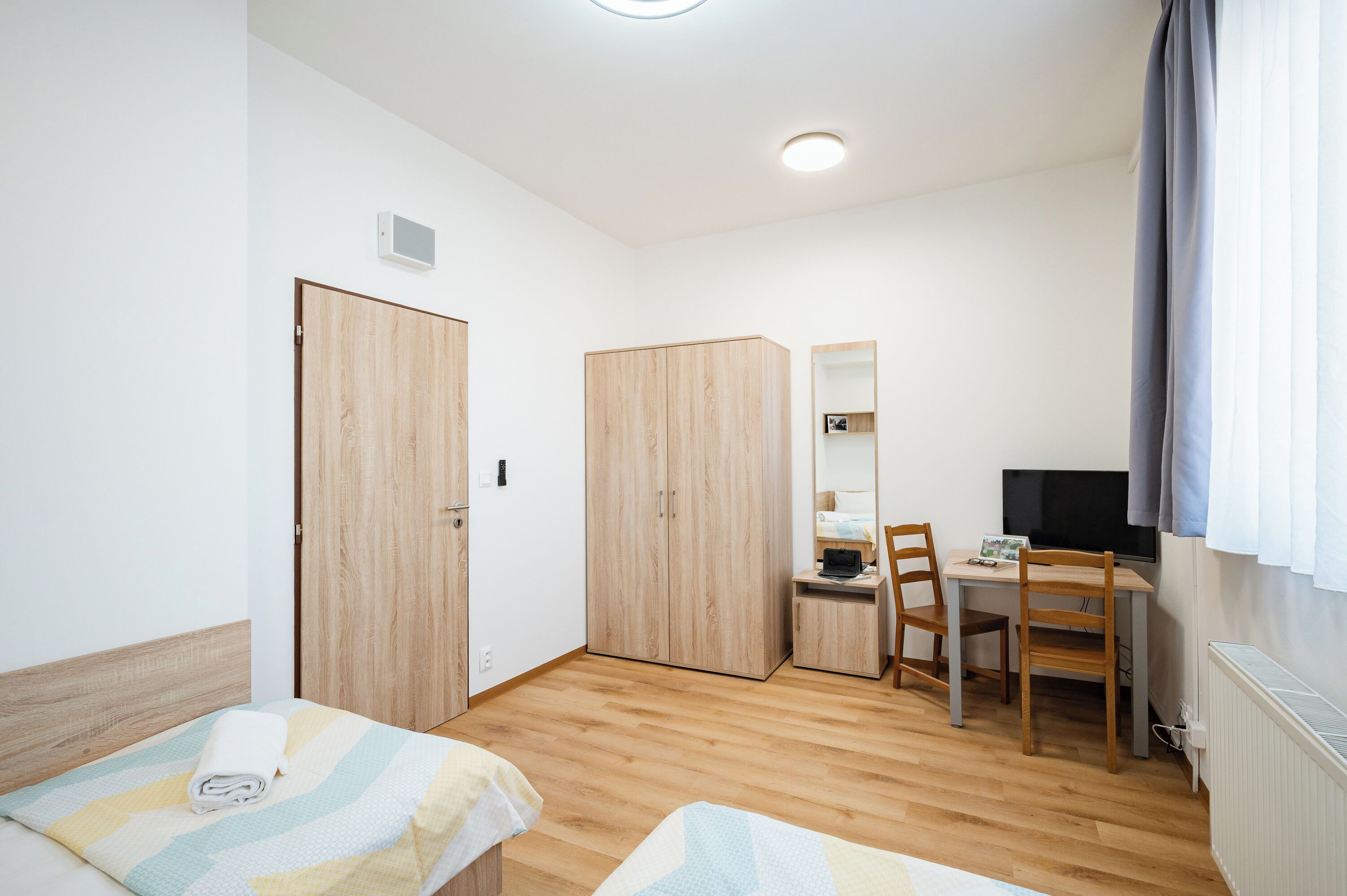 A hotel room with two beds, a desk with a chair, a TV, and a wardrobe.