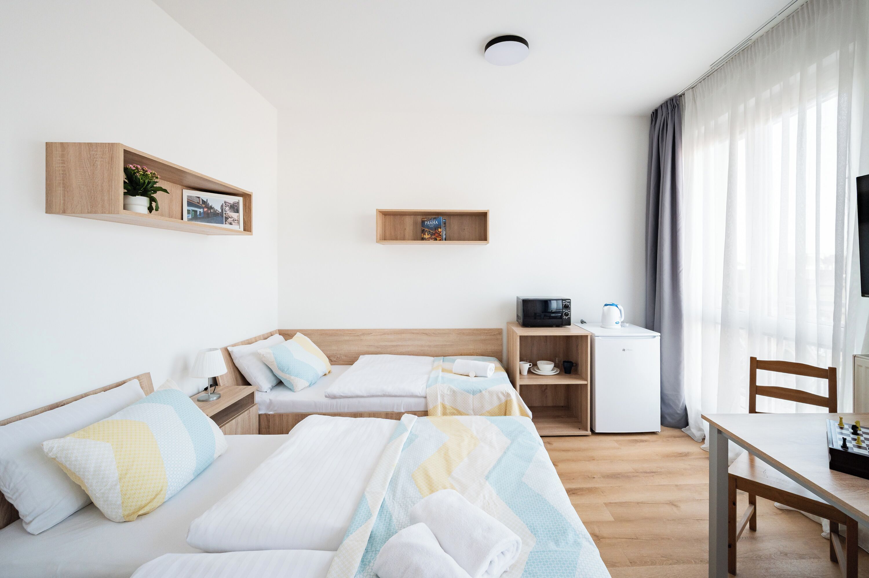 A hotel room with two beds, a desk, a microwave, and a small refrigerator.