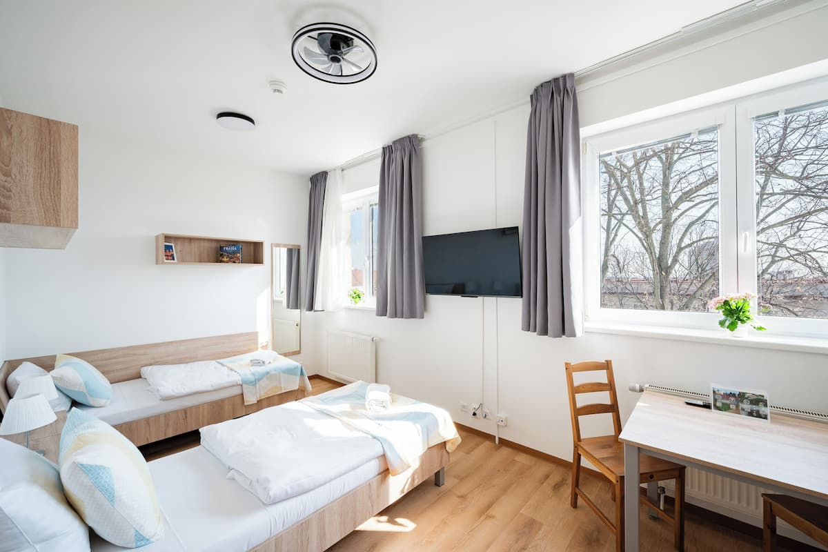 A modern hotel room with two beds, a desk, and a large window with curtains.