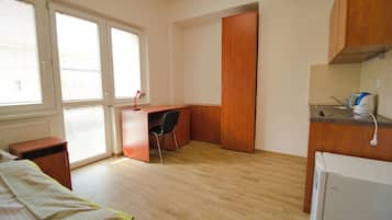 A bedroom with a bed, a desk, a chair, and a kitchenette.
