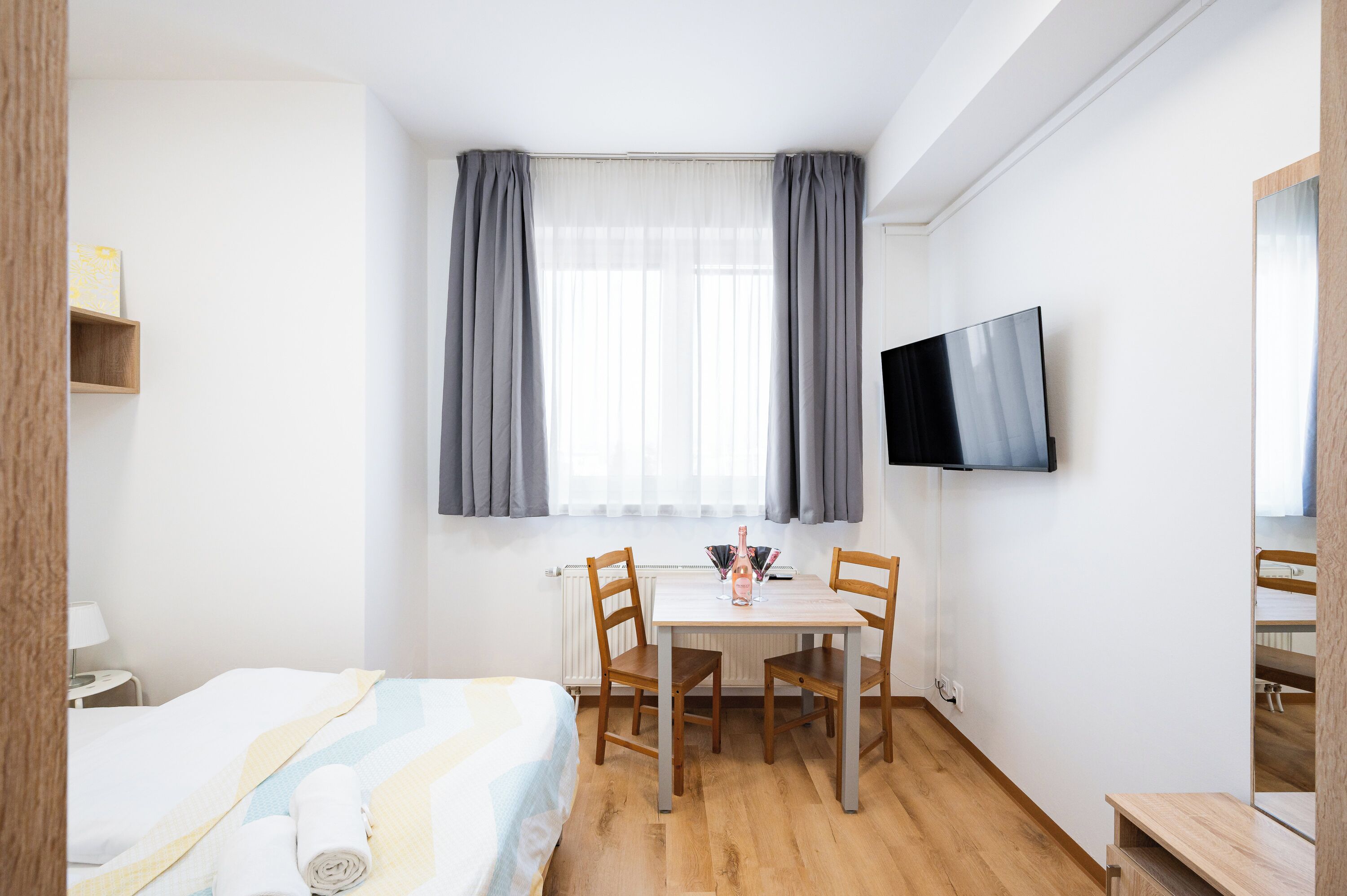 A hotel room with a bed, a desk with two chairs, a TV, and a window with curtains.