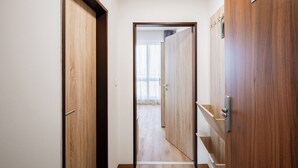 A hallway with wooden doors, a number sign, and a view into a room with a window. - University Hotel (Prague)