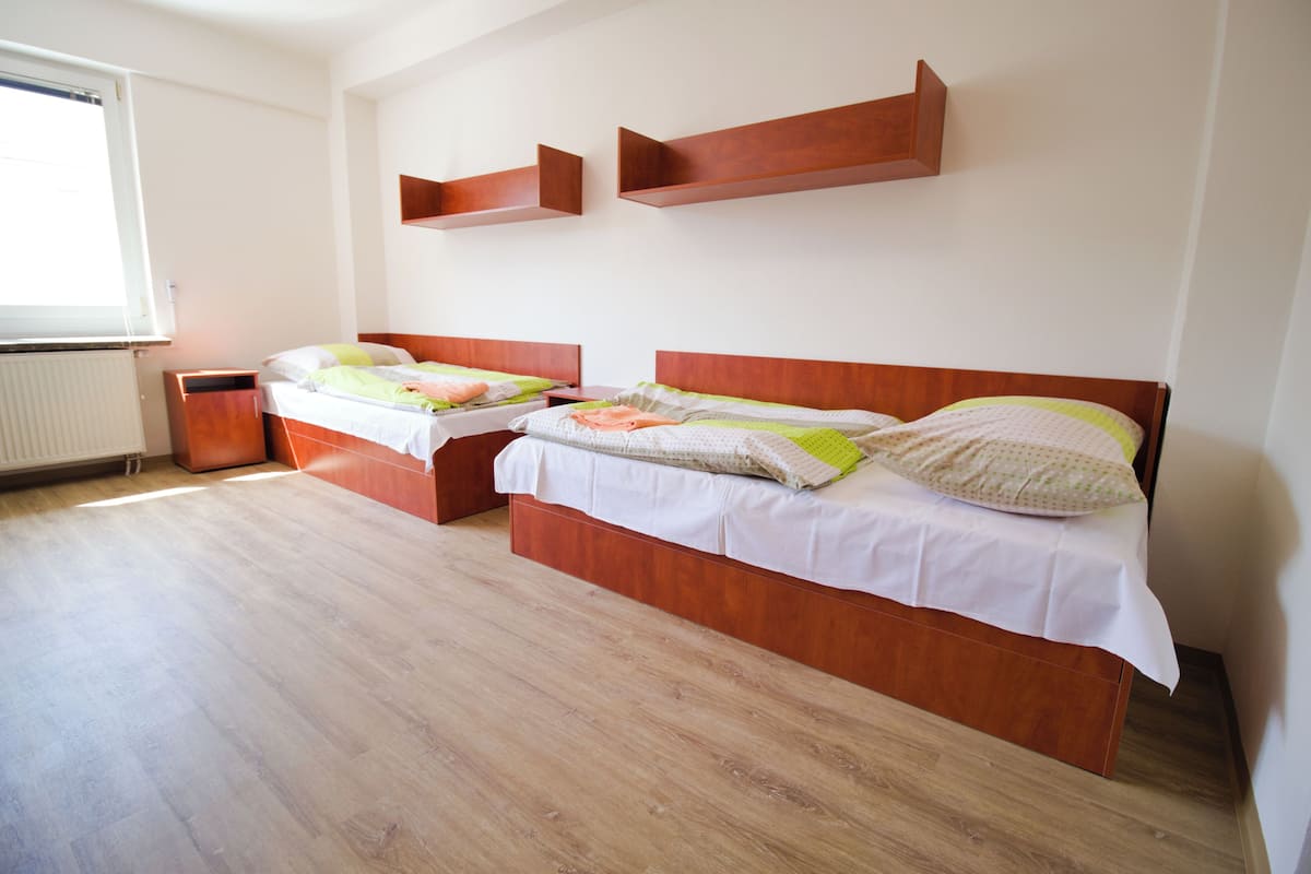 A bedroom with two beds, wooden headboards, a radiator, and a window.
