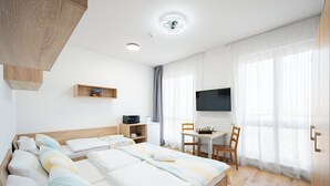 A hotel room with a bed, bedside tables, a desk, a chair, a television, and a window with curtains. - University Hotel (Prague)