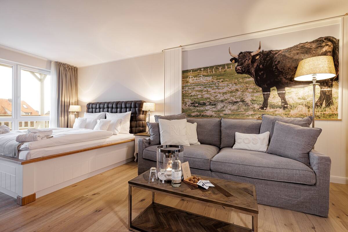 A modern hotel room with a bed, a grey sofa, a coffee table, and a large bull painting on the wall.