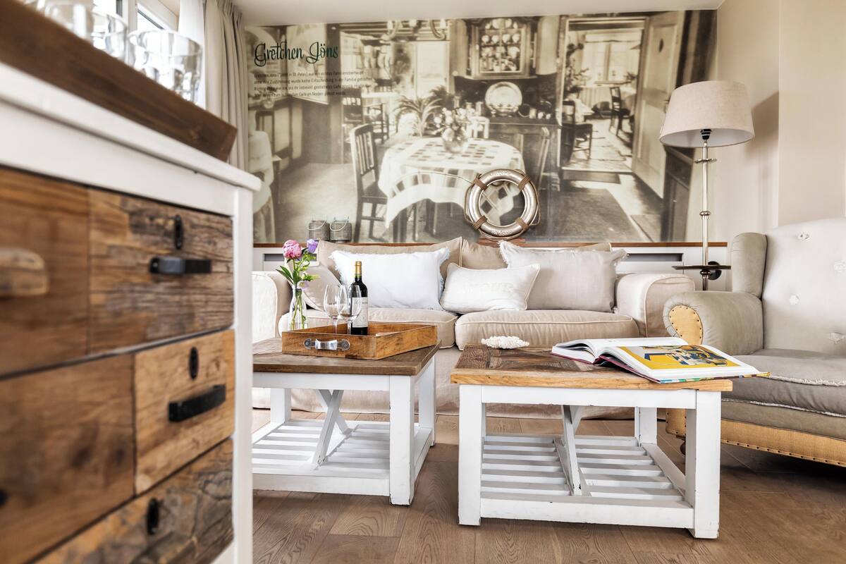 A cozy living room with a large wall mural, white furniture, and a wooden cabinet.
