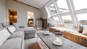 Un salon moderne avec un canapé d’angle, une table basse en bois et une vue sur la ville grâce à de grandes fenêtres.