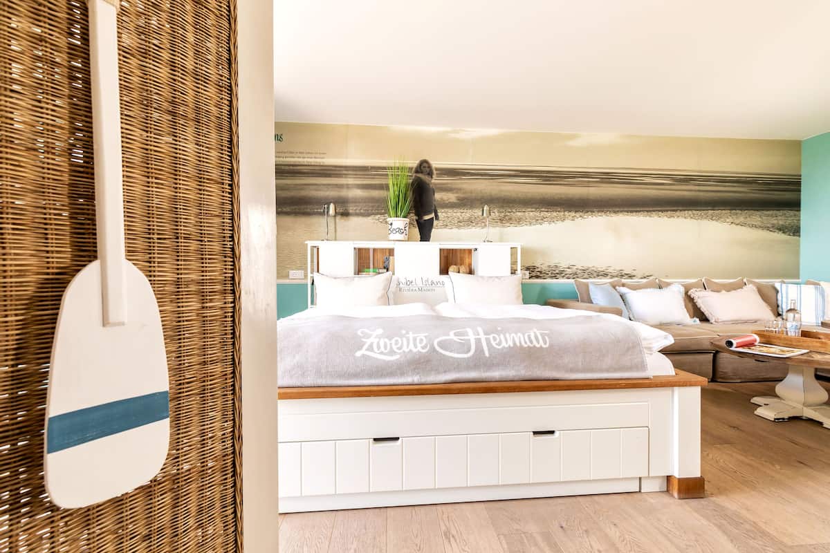 A bedroom with a bed, a sofa, a wall mural, and a plant.