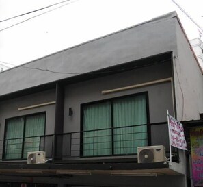 A building with two air conditioning units on the ground floor, large windows with green curtains, and a signboard on the right side. - The 92 residence (Bangkok)