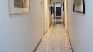 A hallway with a tiled floor, framed artwork on the walls, and recessed lighting. - The 92 residence (Bangkok)