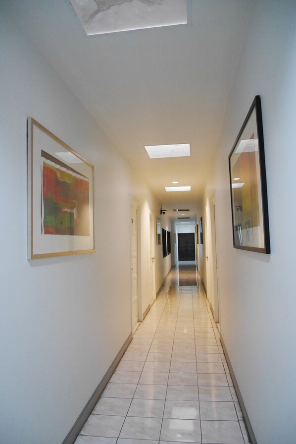 A hallway with a tiled floor, framed artwork on the walls, and recessed lighting. - The 92 residence (Bangkok)
