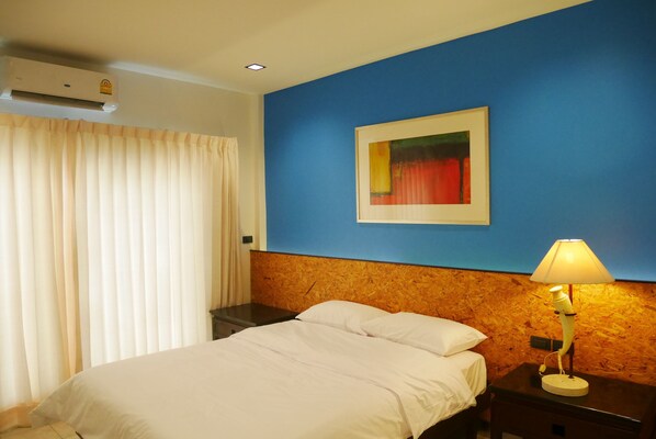 Une chambre d’hôtel avec un lit, une table de chevet avec une lampe, un tableau au mur et un appareil de climatisation.