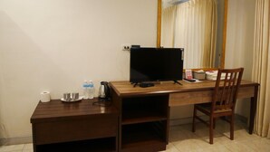 A wooden desk with a flat-screen TV, a chair, a mirror, and a small shelf with toiletries. - The 92 residence (Bangkok)