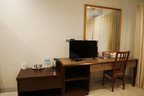 A wooden desk with a flat-screen TV, a chair, a mirror, and a small shelf with toiletries. - The 92 residence (Bangkok)