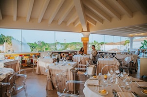 Un restaurante con varias mesas, sillas transparentes y vistas al exterior con vegetación.